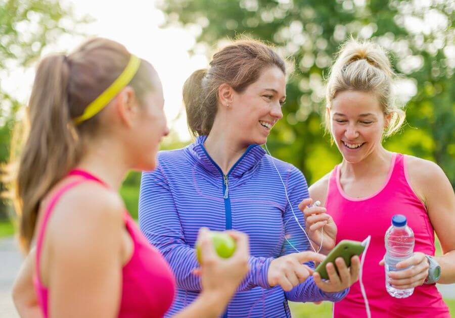Group of happy active girls preparing for a run in nature by choosing music on a smart phone