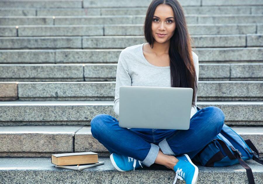 Portrait of a happy young woman sitting on the city stairs and using laptop computer outdoors
