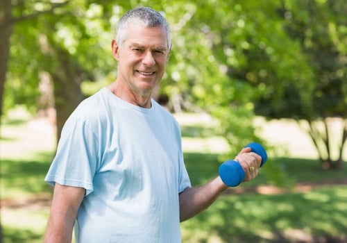 Portrait of a smiling mature man exercising with dumbbell at the park